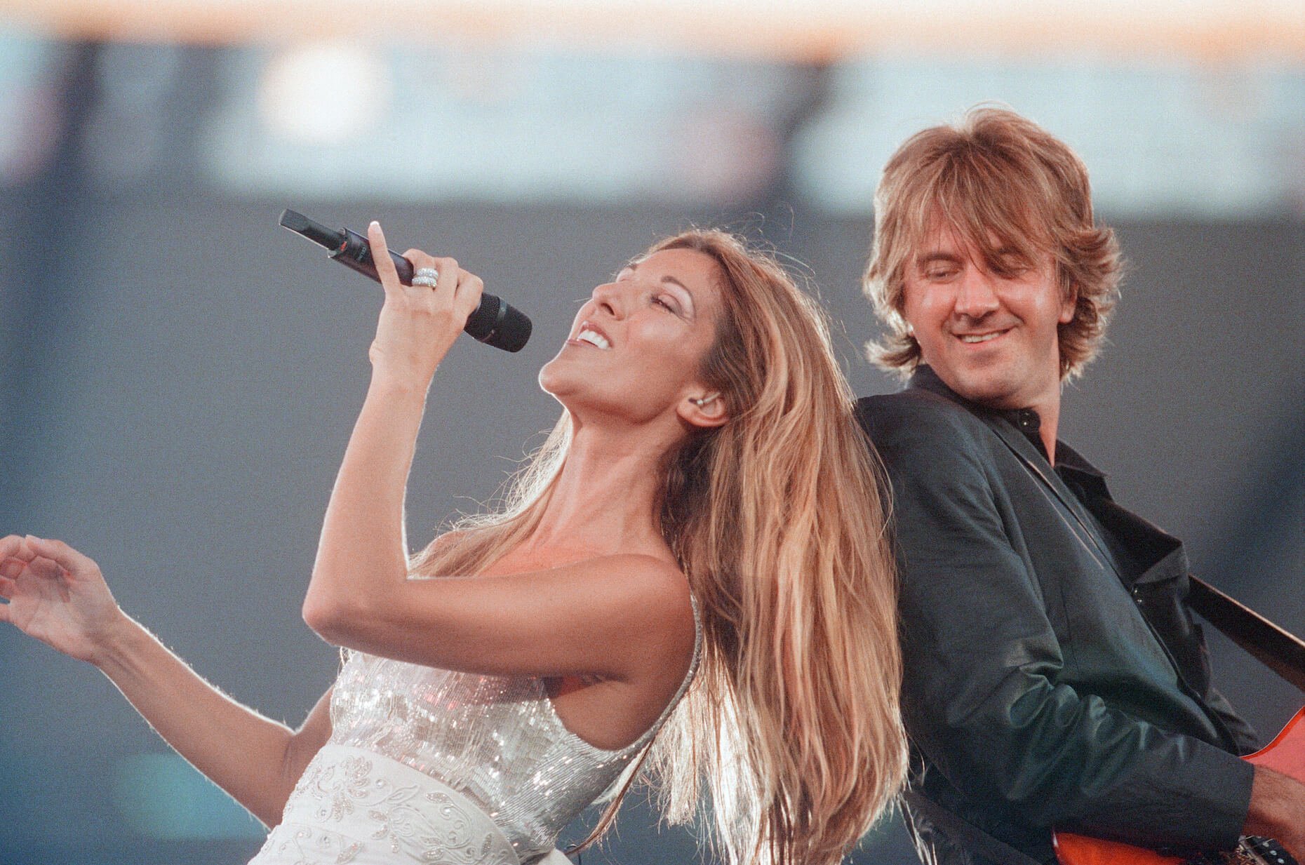 Celine Dion singing on stage with her back against a guitar player