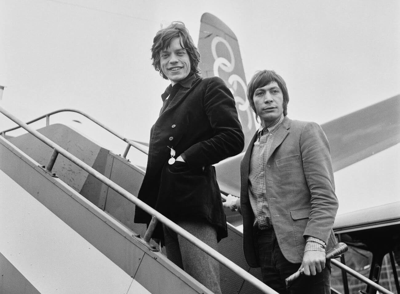 A black and white picture of Mick Jagger and Charlie Watts on the stairs leading up to an airplane.