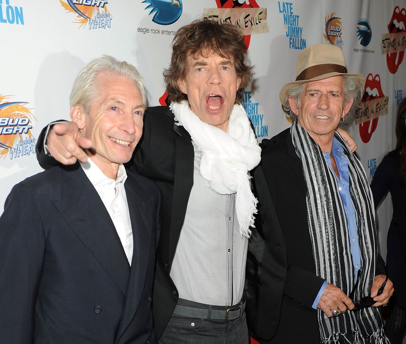 Charlie Watts, Mick Jagger, and Keith Richards pose together. Jagger puts his arms around his bandmates' shoulders.