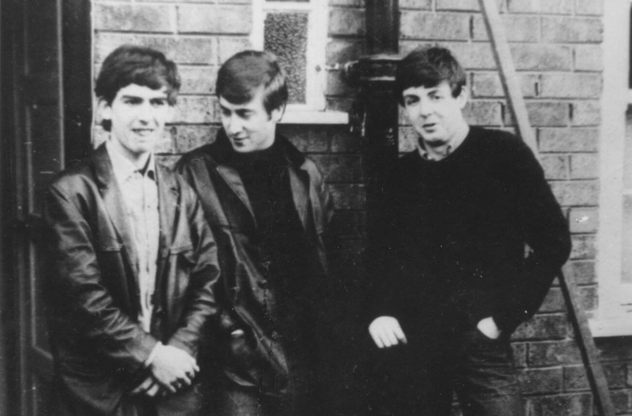 A black and white picture of George Harrison, John Lennon, and Paul McCartney standing in front of a brick wall.
