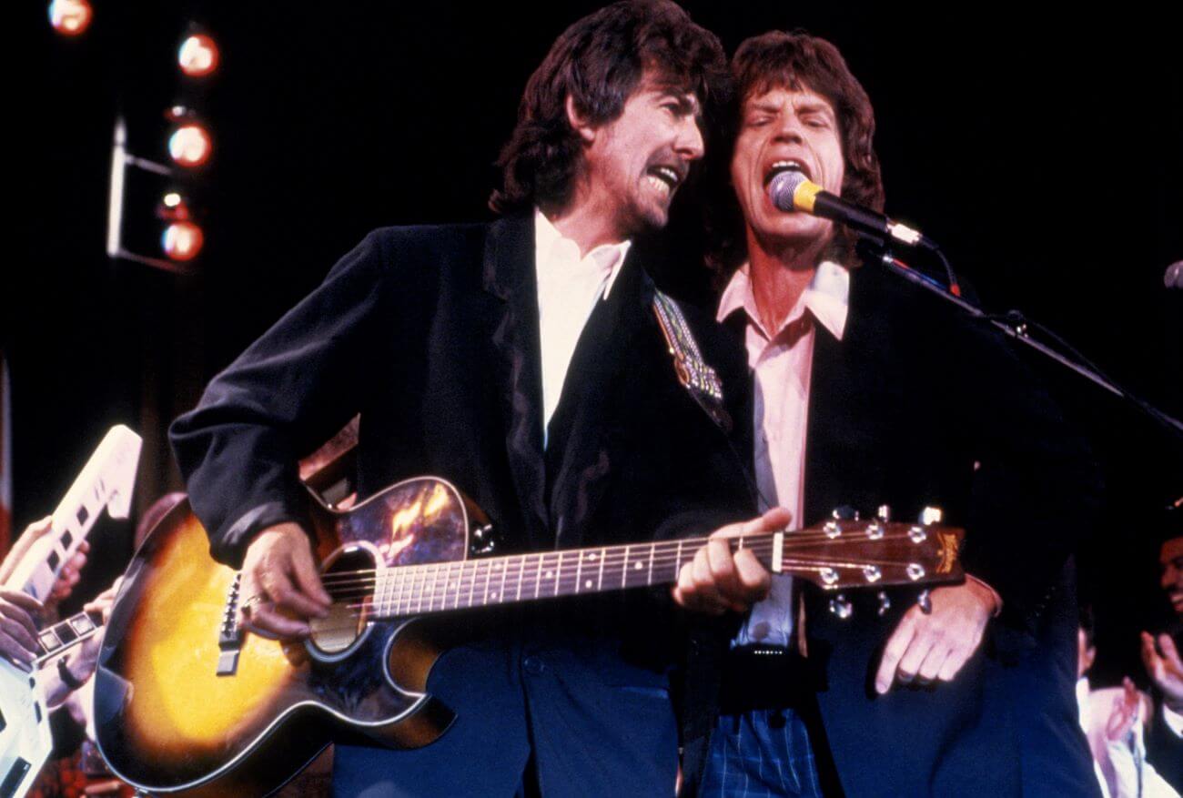 George Harrison plays guitar and sings into a microphone with Mick Jagger.