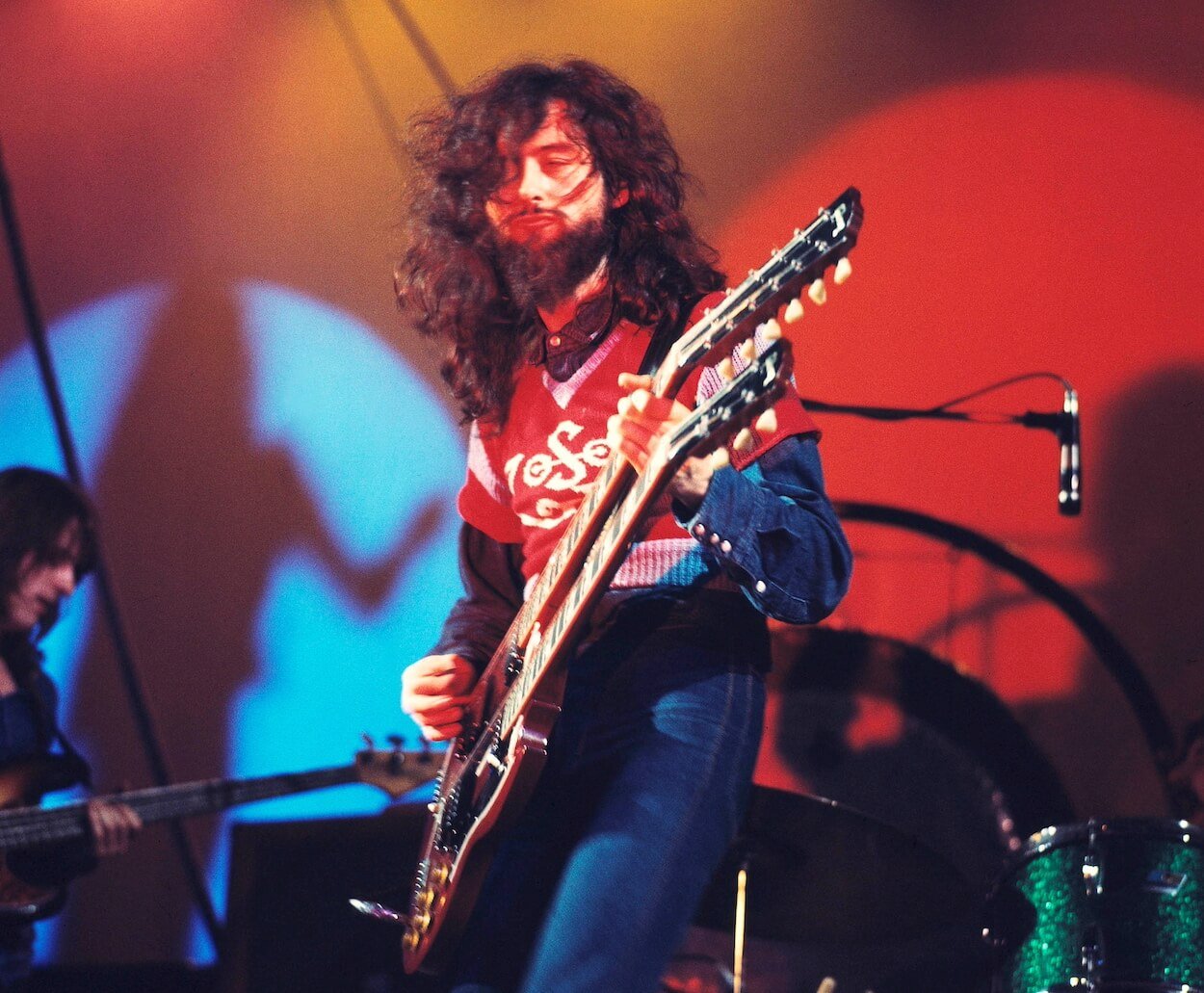Led Zeppelin's Jimmy Page playing a double-necked guitar and standing in front of a multi-colored background during a 1971 concert.