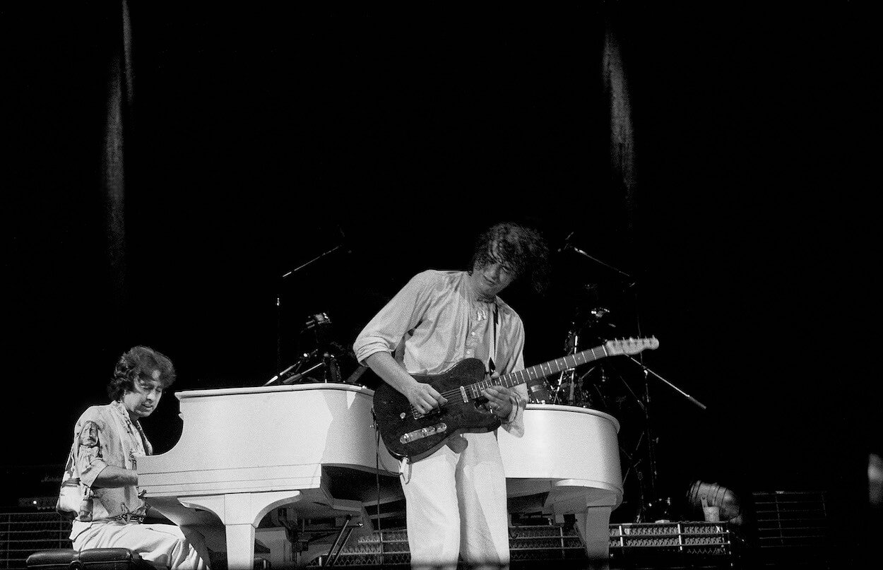 Jimmy Page (right) playing guitar in front of Paul Rodgers playing a piano during a 1985 concert by their band The Firm.