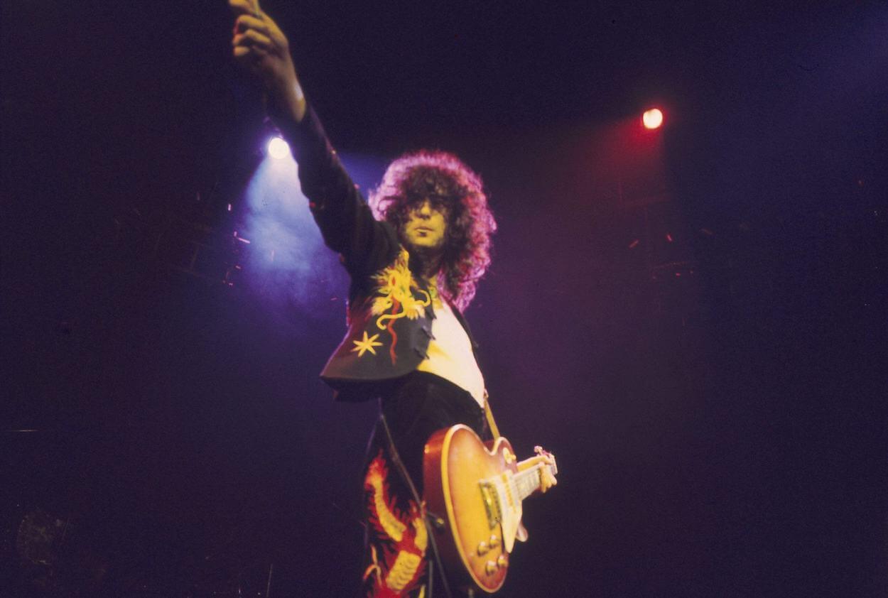 Jimmy Page raising his right hand in the air while playing guitar during a 1975 Led Zeppelin concert.
