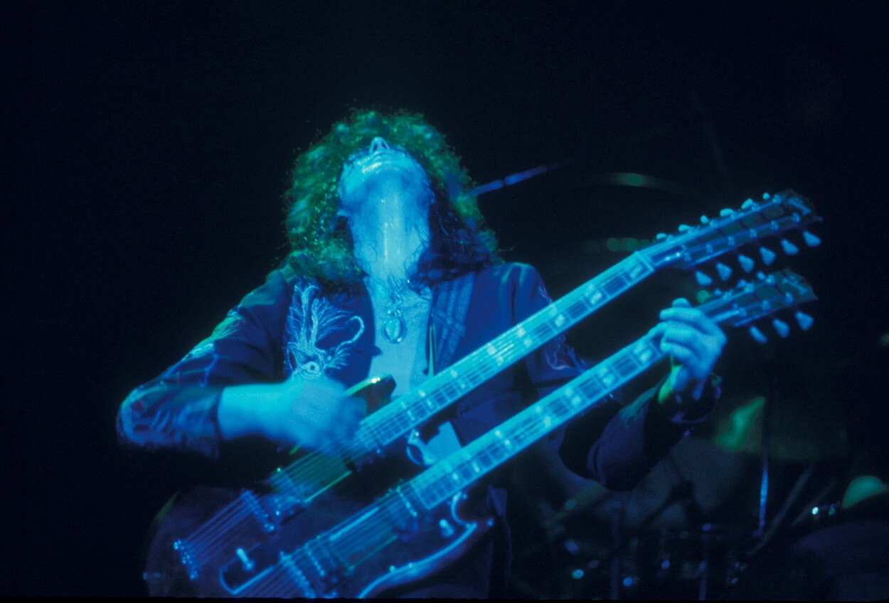 Jimmy Page looking upward as he plays a double-necked guitar during a 1975 Led Zeppelin concert.