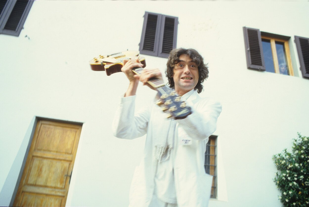 Jimmy Page wearing a white suit and pretending to swing his guitar like an axe.