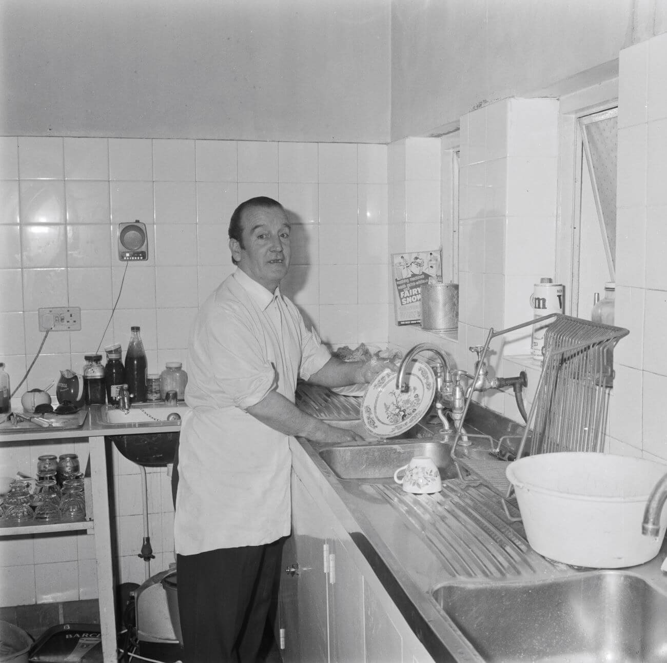 A black and white picture of John Lennon's father Alfred standing at a sink washing a plate.