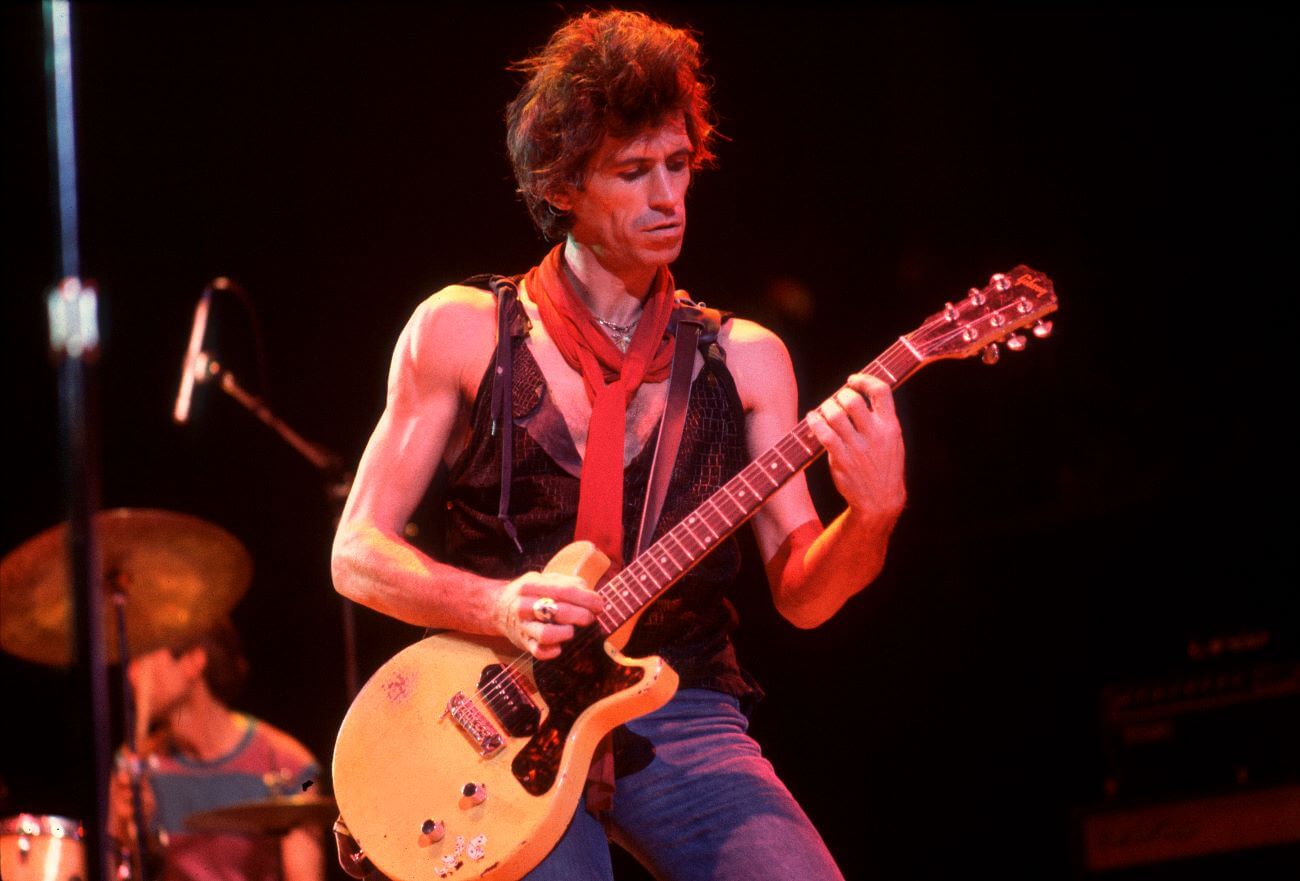 Keith Richards wears a black tank top and plays guitar.