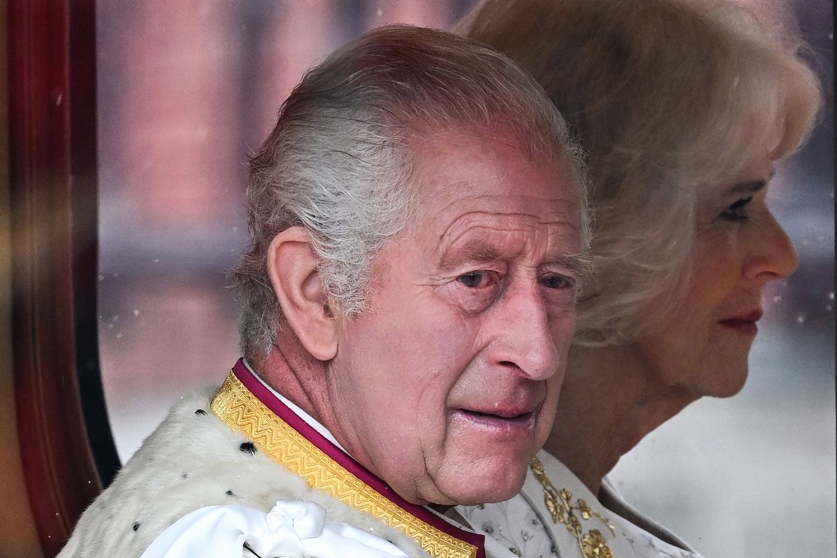 King Charles faces the camera with Queen Camilla in the background
