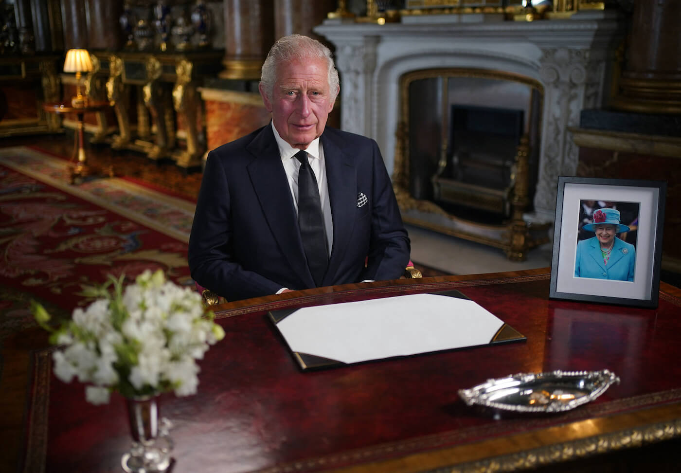 King Charles III sitting at a desk in a suit
