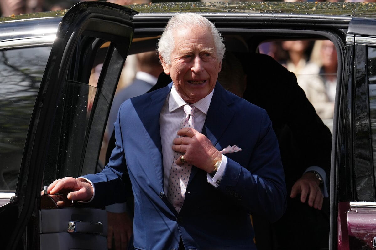 King Charles, whose coronation cost includes millions spent of security, per experts, exits a vehicle and adjusts his tie