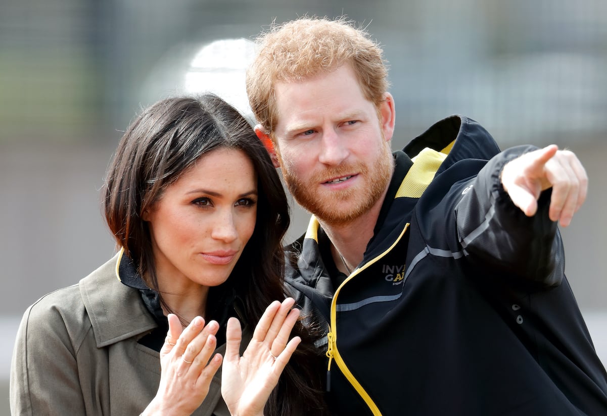 Prince Harry points at something while Meghan Markle looks on