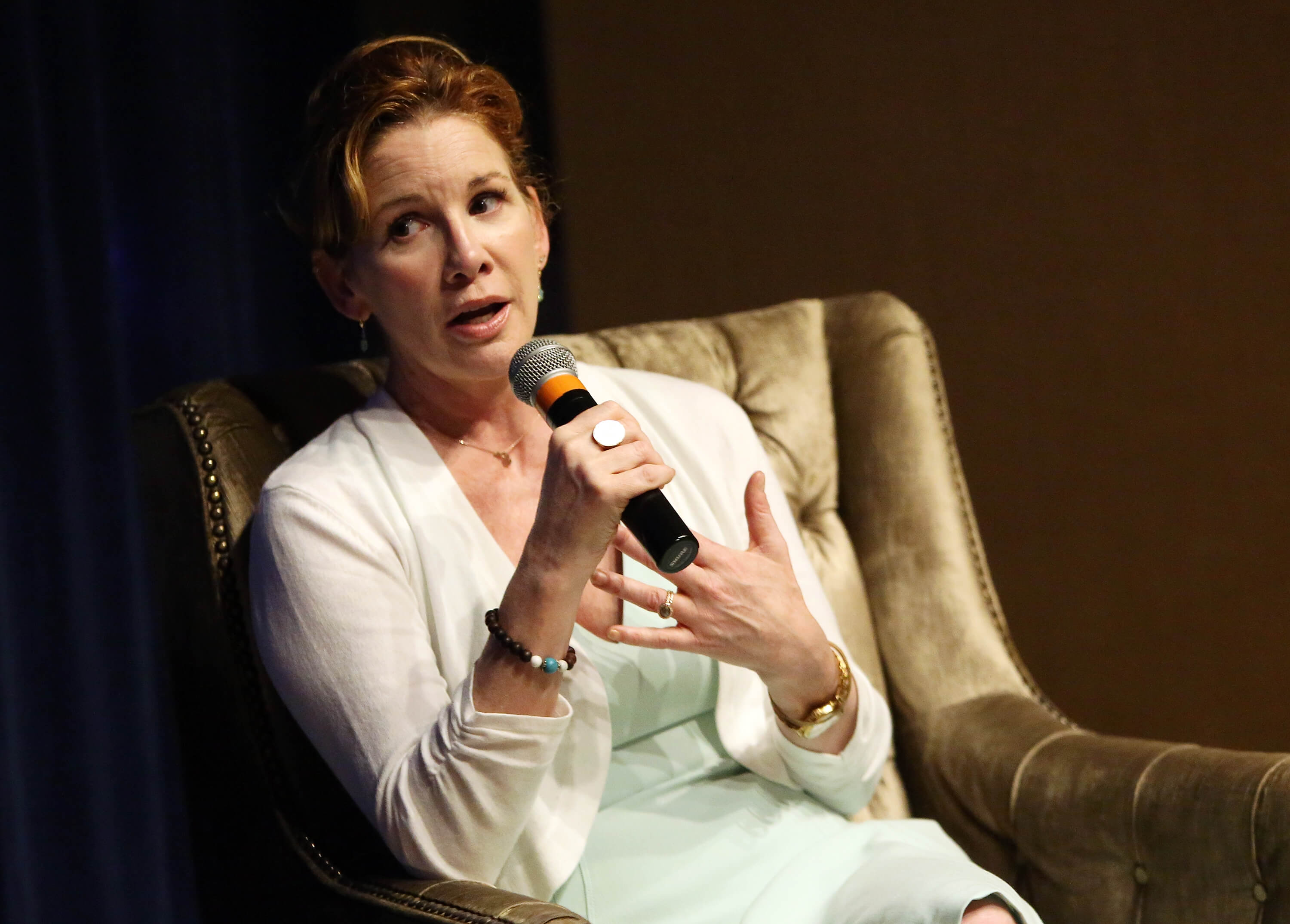 Melissa Gilbert speaks into a mic while sitting in a chair. 