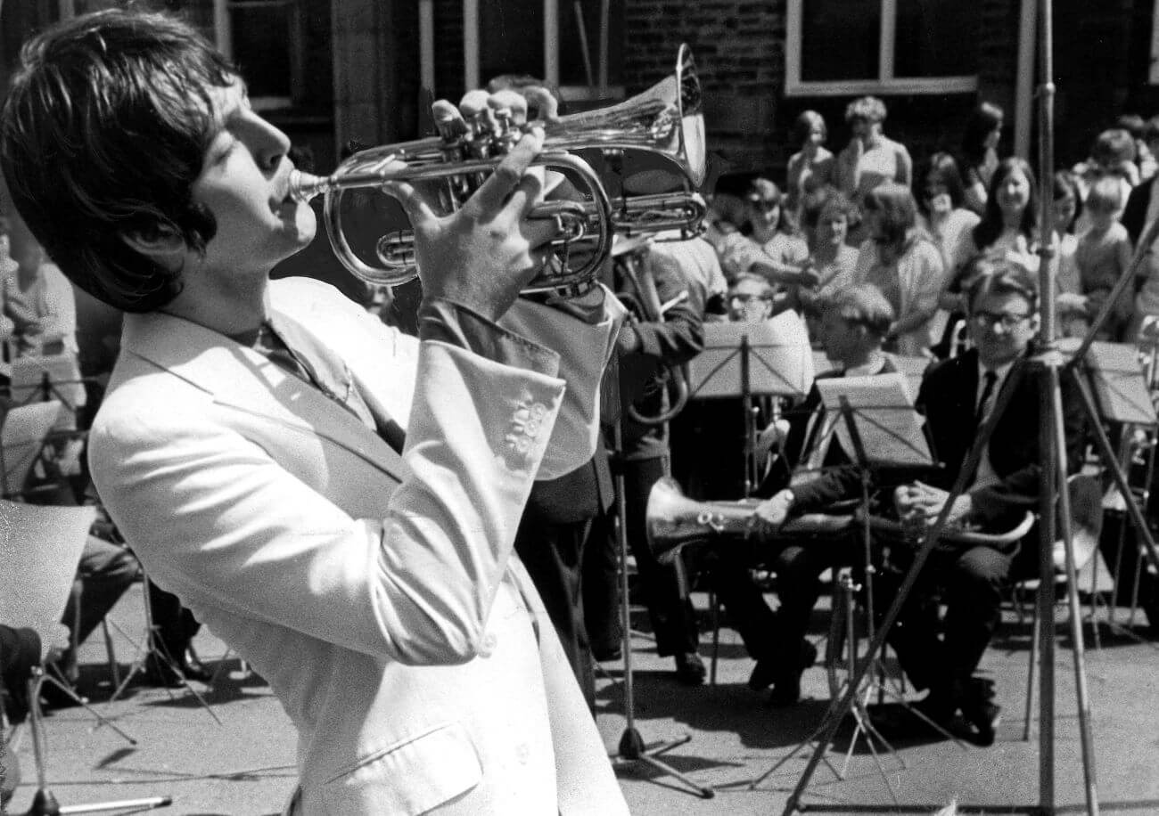 A black and white picture of Paul McCartney playing trumpet in front of a crowd of people.