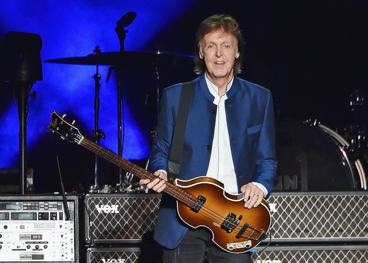 Paul McCartney wearing a blue suit and holding a bass guitar.
