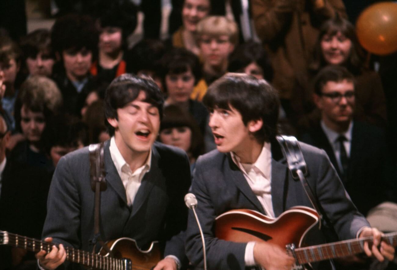 Paul McCartney and George Harrison play guitars and sing into the same microphone.