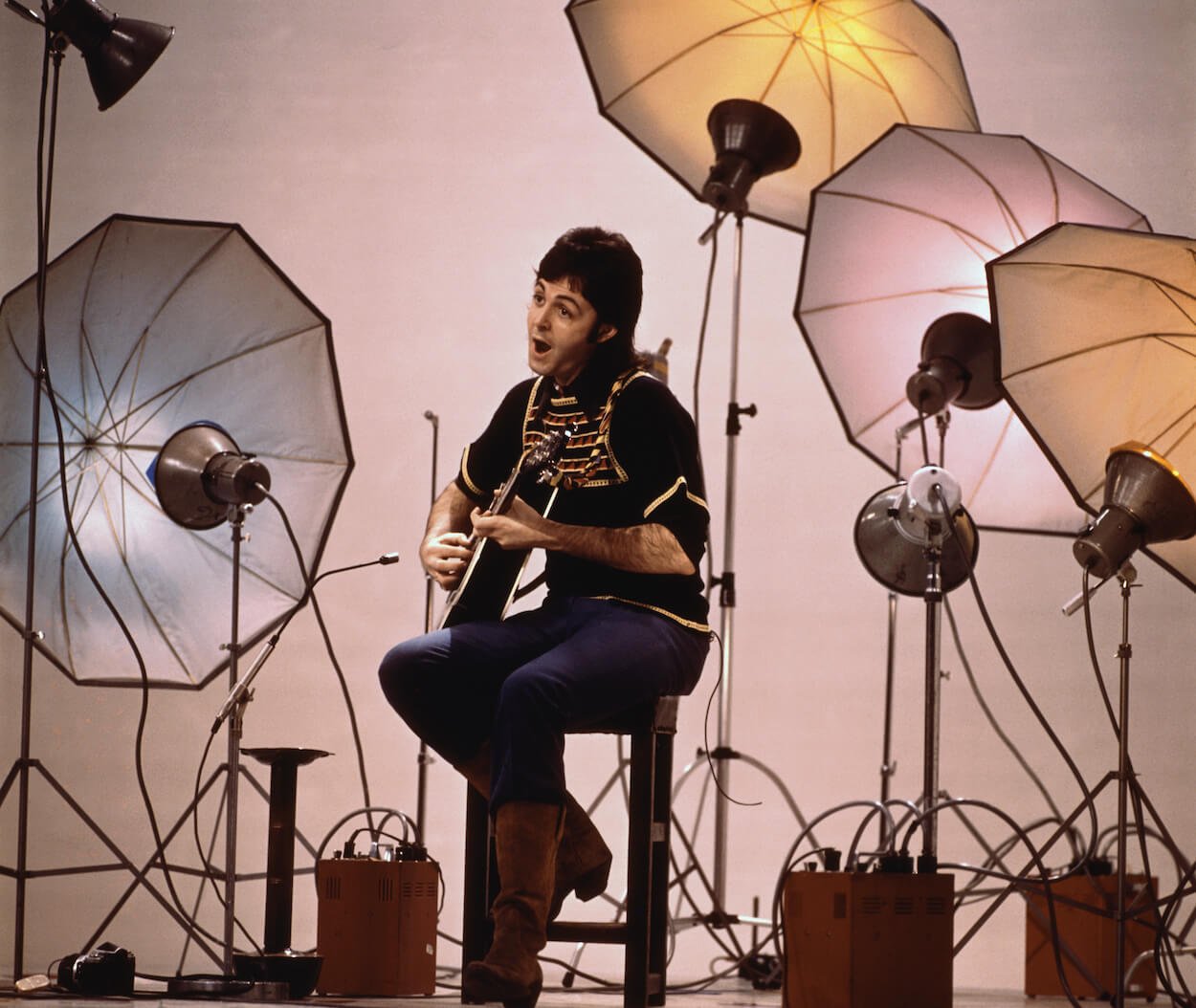 Paul McCartney sitting on a stool playing acoustic guitar during an April 1972 TV special in which he performed the James Bond theme song 'Live and Let Die.'