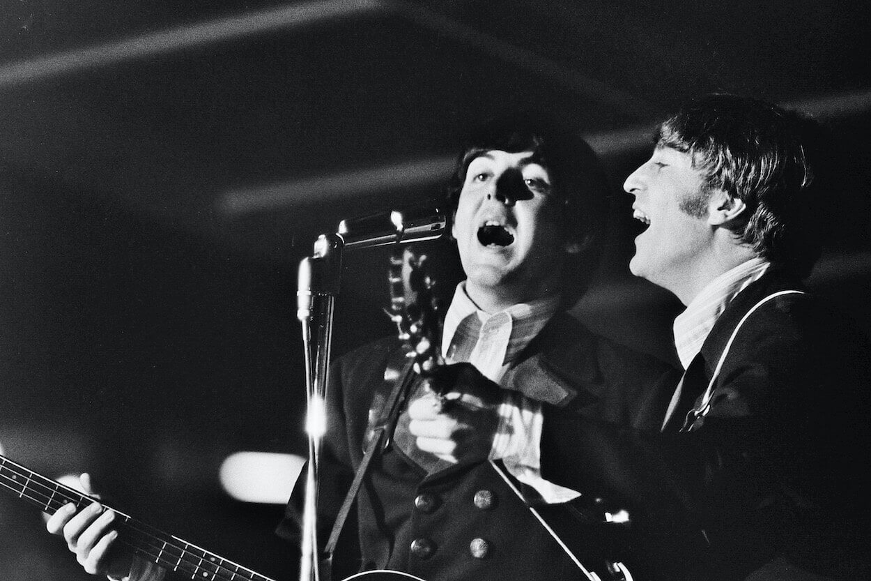 Paul McCartney (left) and John Lennon sing into a shared microphone during a 1966 concert in St. Louis.