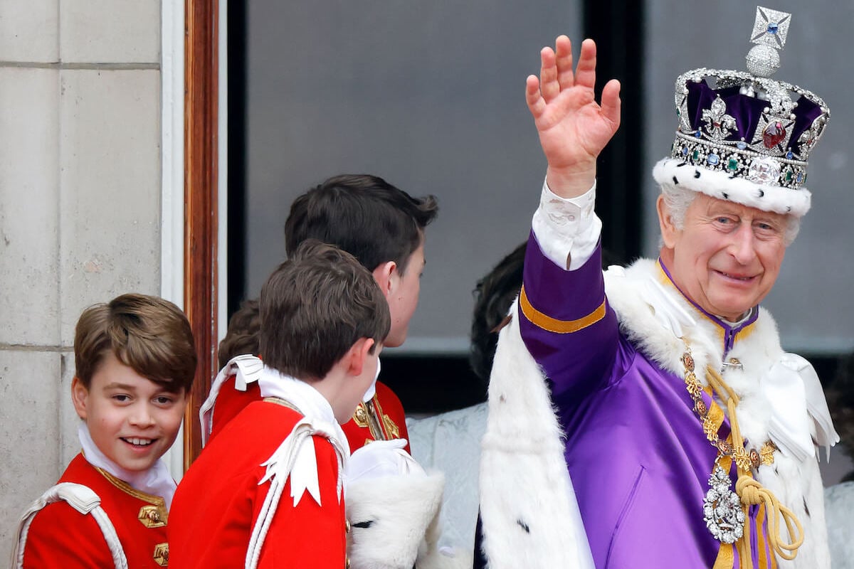 King Charles III, whose conversation with Queen Camilla on the Buckingham Palace balcony a lip reader decoded, waves while standing near Prince George