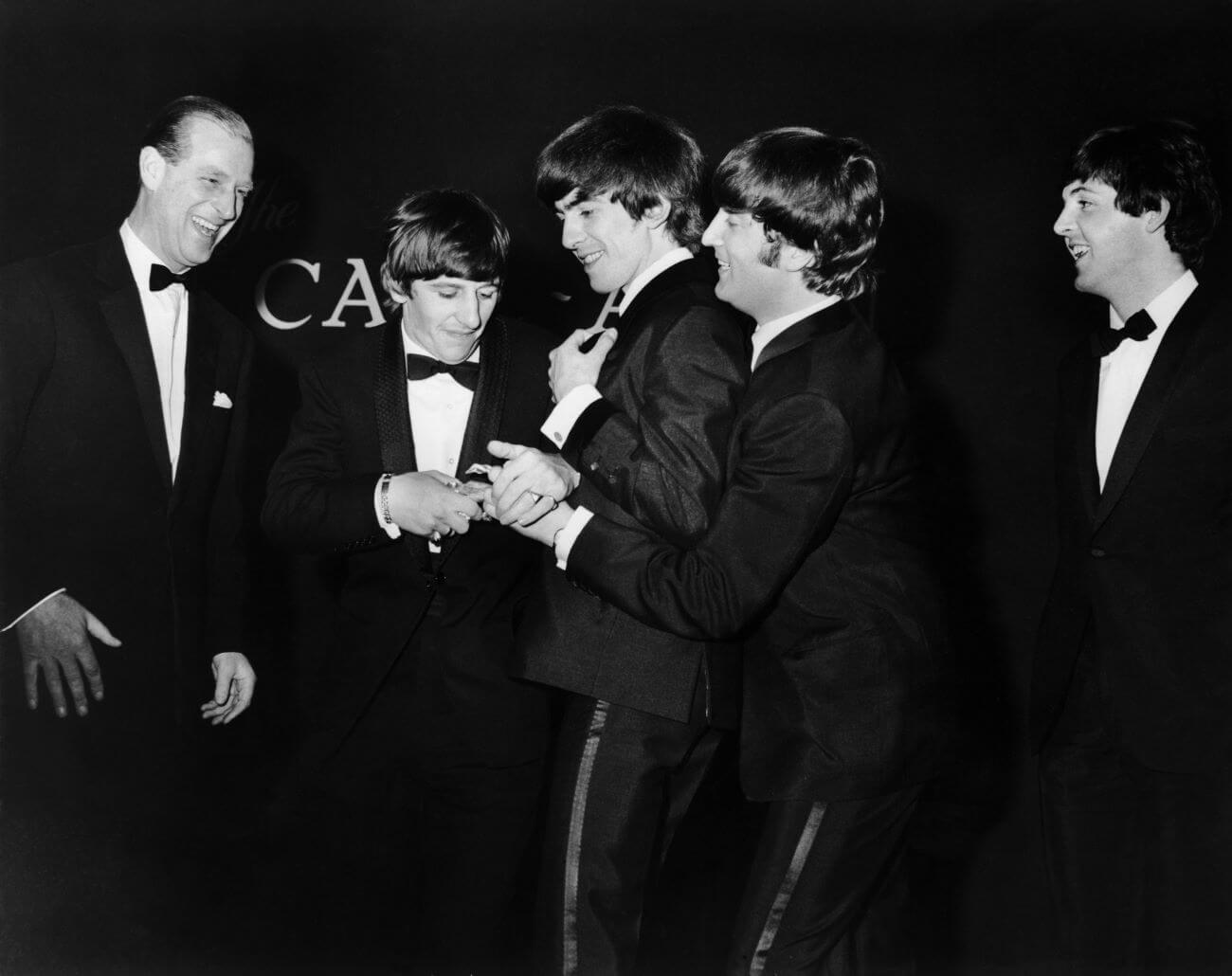 A black and white picture of Prince Philip, Ringo Starr, George Harrison, John Lennon, and Paul McCartney wearing tuxedos.