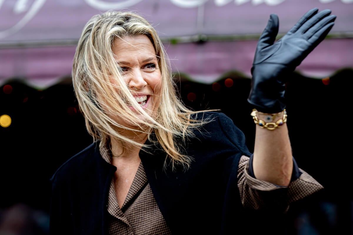 Queen Maxima, wearing a gold bracelet and black glove, smiles and waves.
