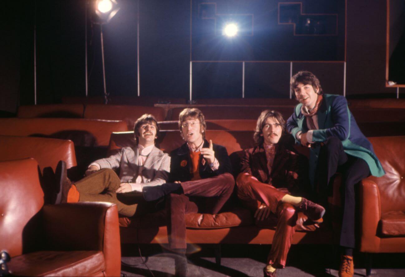 Ringo Starr, John Lennon George Harrison, and Paul McCartney of The Beatles sit on chairs in a theater.