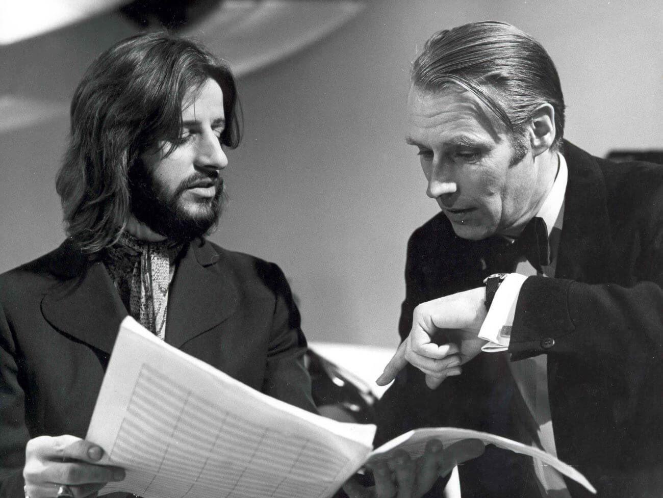 A black and white picture of Ringo Starr and George  Martin looking at a packet of paper.