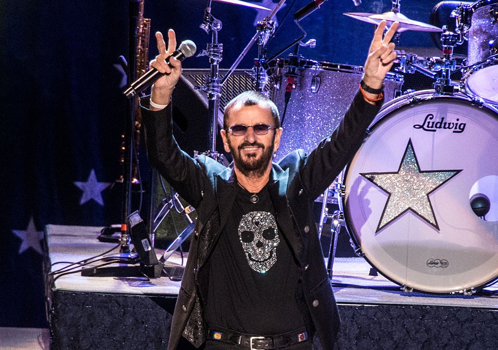 Ringo Starr flashing two peace signs on stage.