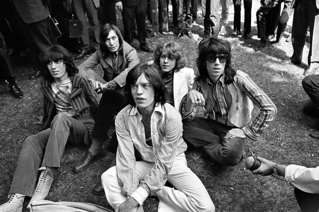 Rolling Stones members (from left) Bill Wyman, Charlie Watts, Mick Jagger, Mick Taylor, and Keith Richards sitting in the grass surrounded by press.