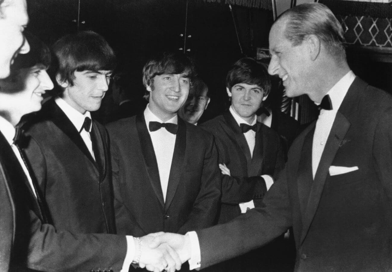 A black and white picture of Prince Philip shaking hands with Ringo Starr while George Harrison, John Lennon, and Paul McCartney watch.