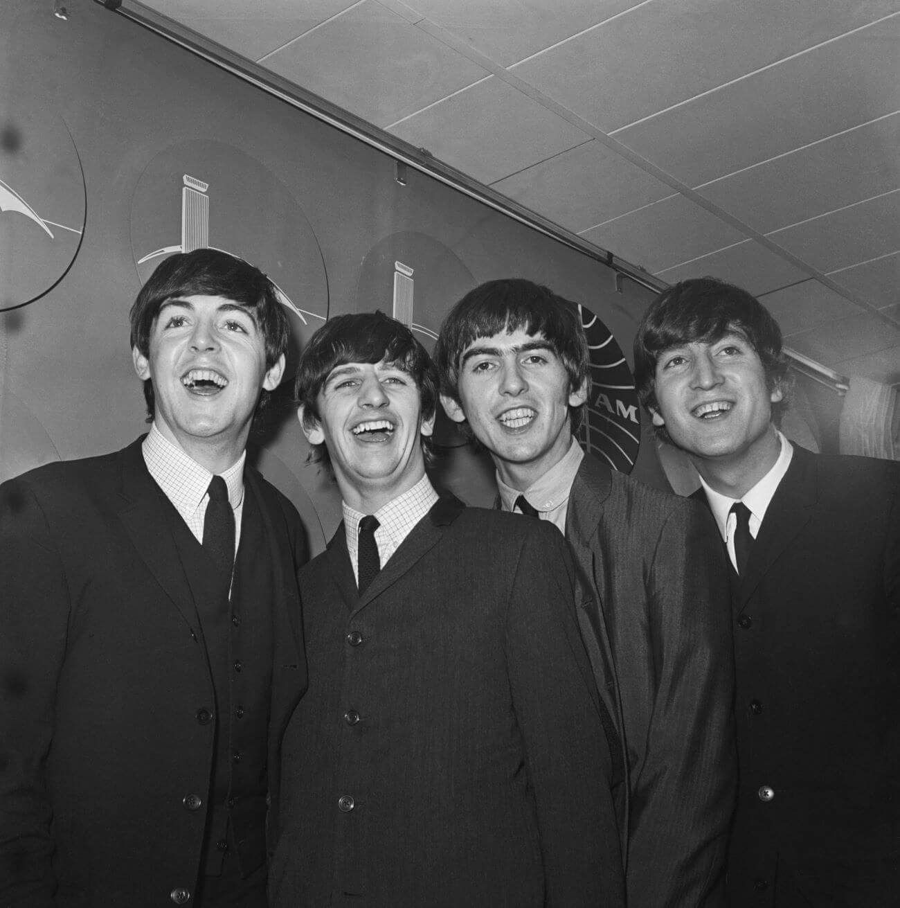 A black and white picture of Paul McCartney, Ringo Starr, George Harrison, and John Lennon wearing suits and smiling.