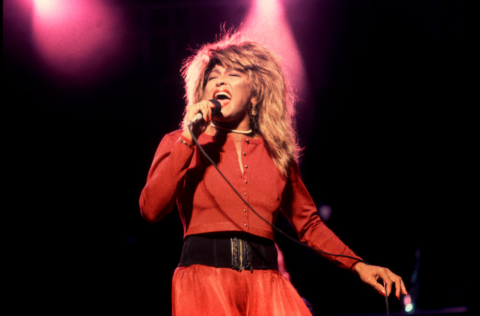 Tina Turner singing on stage in a red outfit