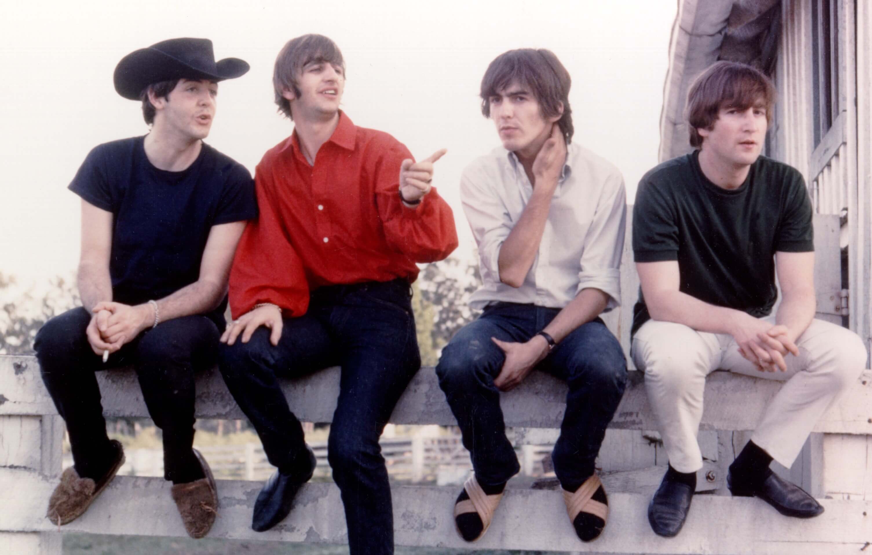 Paul McCartney, Ringo Starr, George Harrison, and John Lennon sitting on a fence during The Beatles' "Help!" era