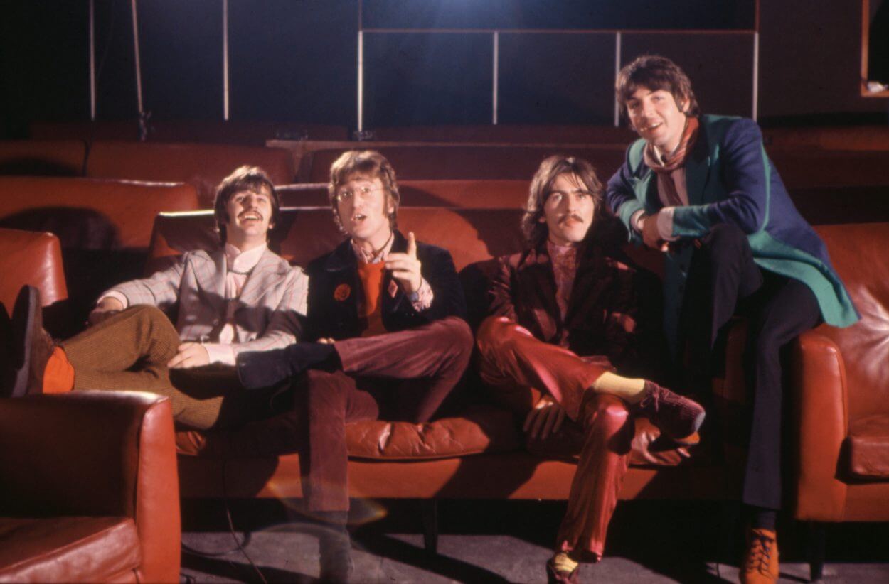 Beatles members (from left) Ringo Starr, John Lennon, George Harrison, and Paul McCartney sitting together on red chairs in a film screening room.