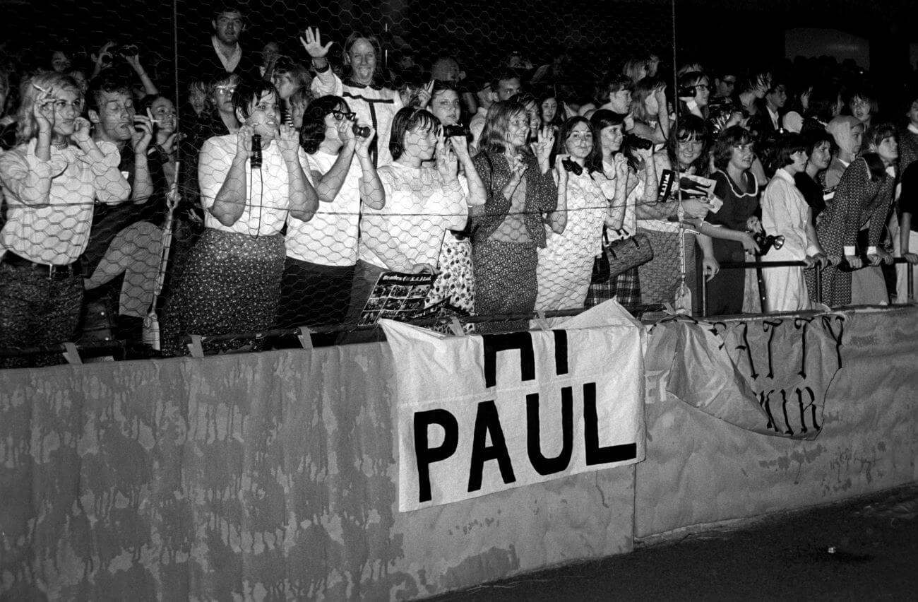 A black and white picture of Beatles fans leaning up against netting at a concert.