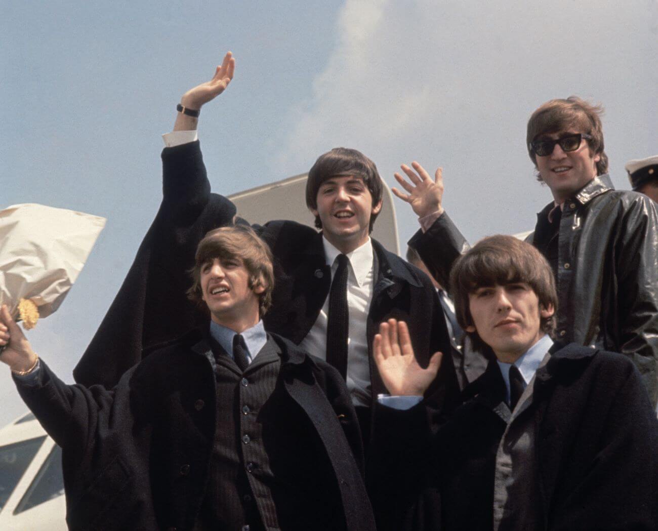 Ringo Starr, Paul McCartney, George Harrison, and John Lennon of The Beatles wave from the door of an airplane.