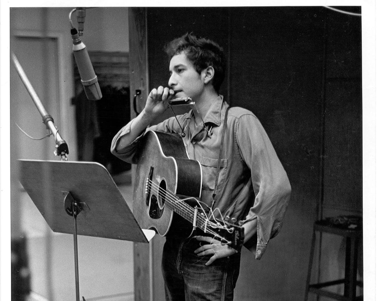 A black and white picture of Bob Dylan playing guitar and standing in front of a music stand.