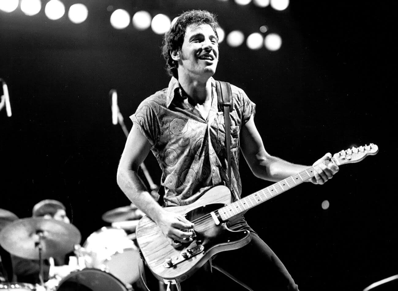 A black and white picture of Bruce Springsteen on a stage playing guitar.
