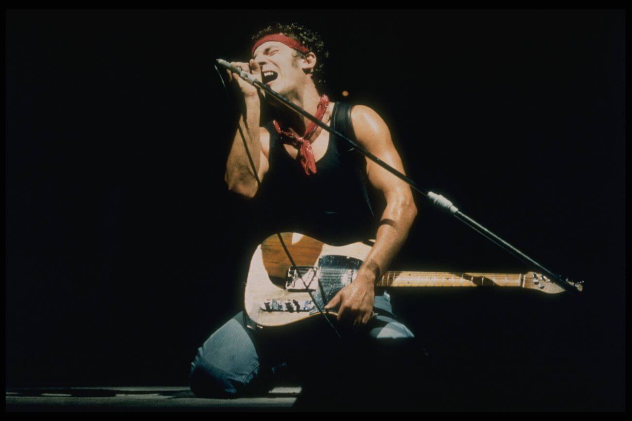 Bruce Springsteen sings into a microphone while holding a guitar.