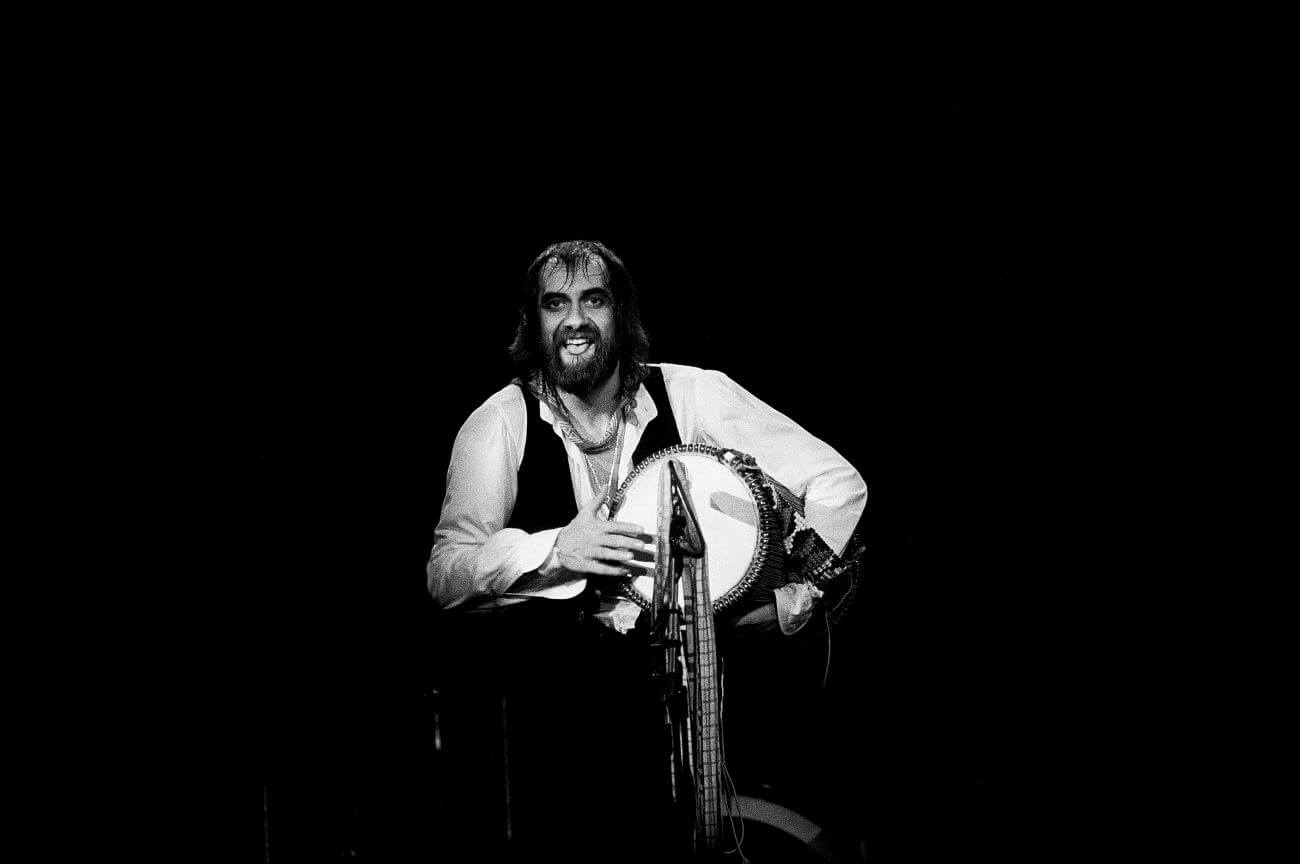 A black and white picture of Mick Fleetwood playing a drum onstage.