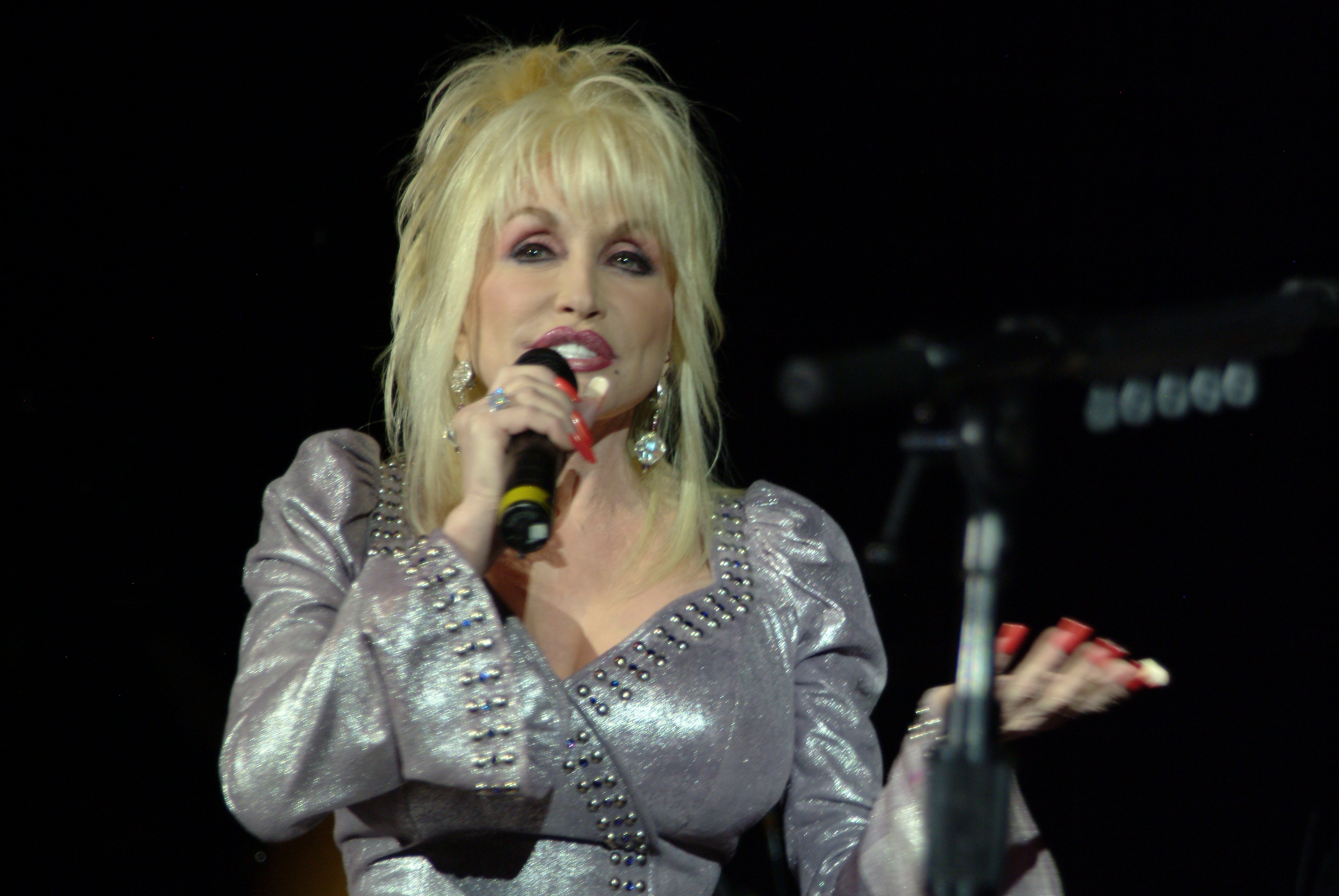Dolly Parton speaking into a microphone in a silver outfit.