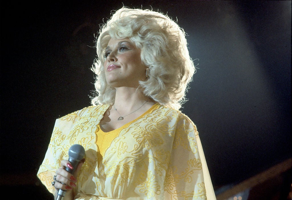 Dolly Parton on stage in a yellow outfit with a microphone in hand.