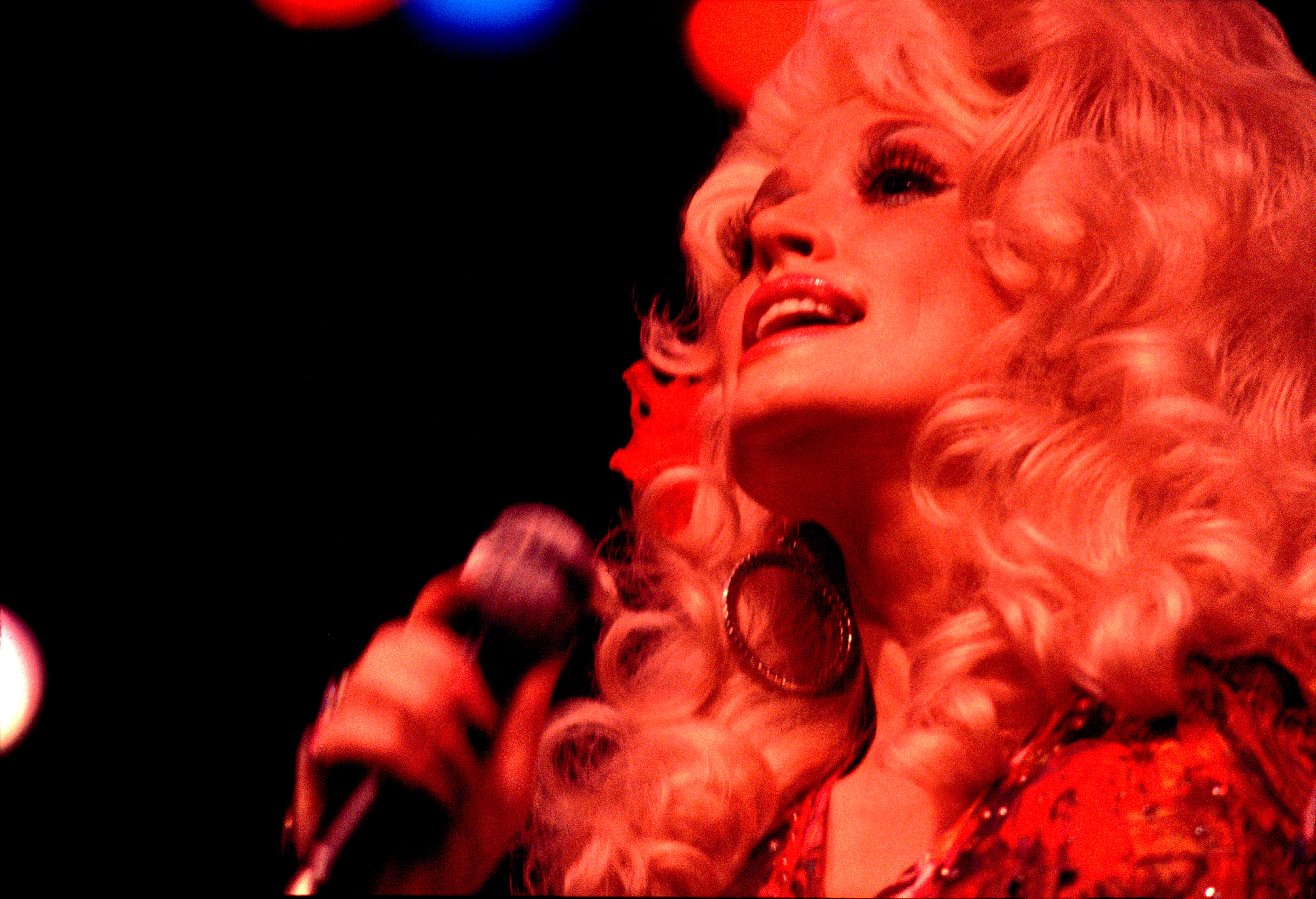 Dolly Parton singing onstage in red light.