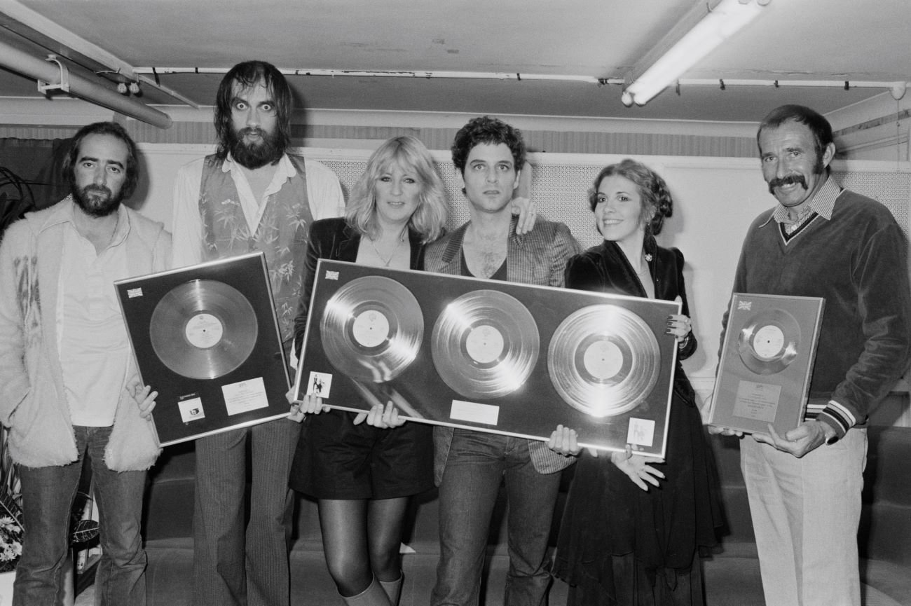 John McVie, Mick Fleetwood, Christine McVie, Lindsey Buckingham, Stevie Nicks, and a friend hold framed records.