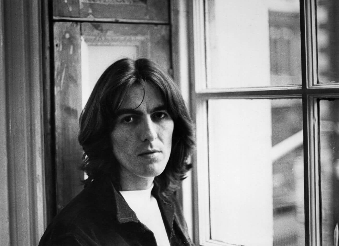 A black and white picture of Beatles guitarist George Harrison standing next to a window.
