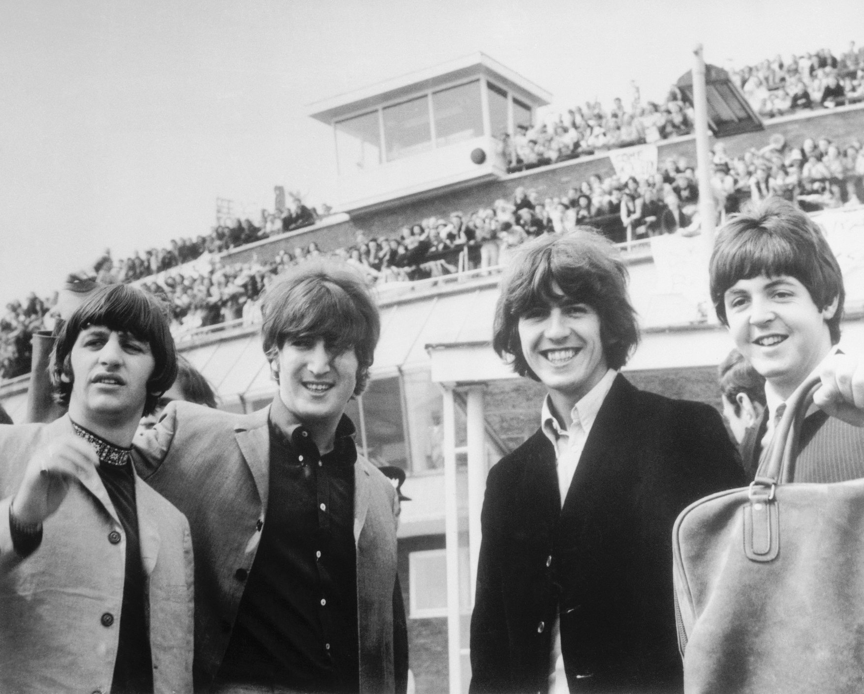 The Beatles (Ringo Starr, John Lennon, George Harrison, and Paul McCartney) pose in front of fans at London airport