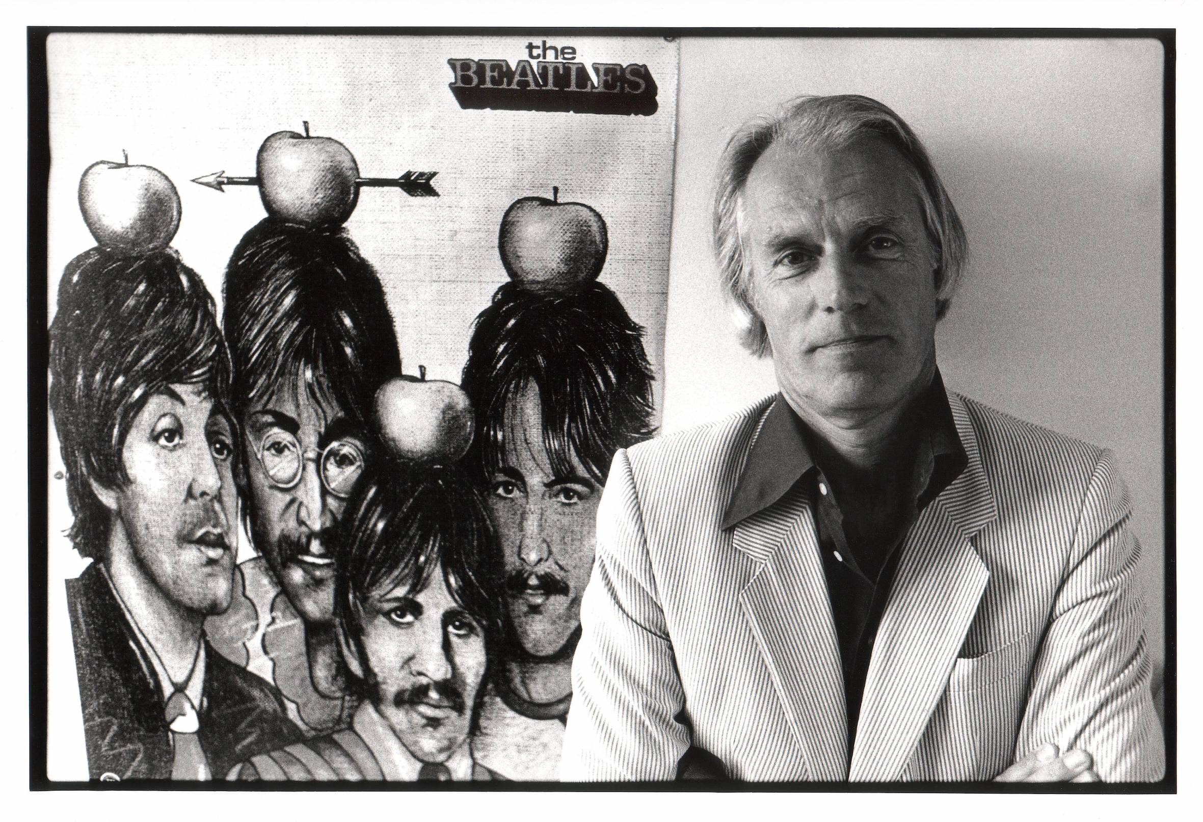 Producer George Martin poses in front of a poster of The Beatles