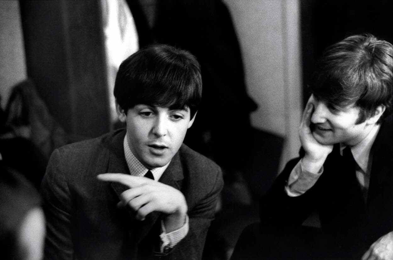 Paul McCartney (left) pointing to his right while John Lennon watches before a December 1963 concert in London.