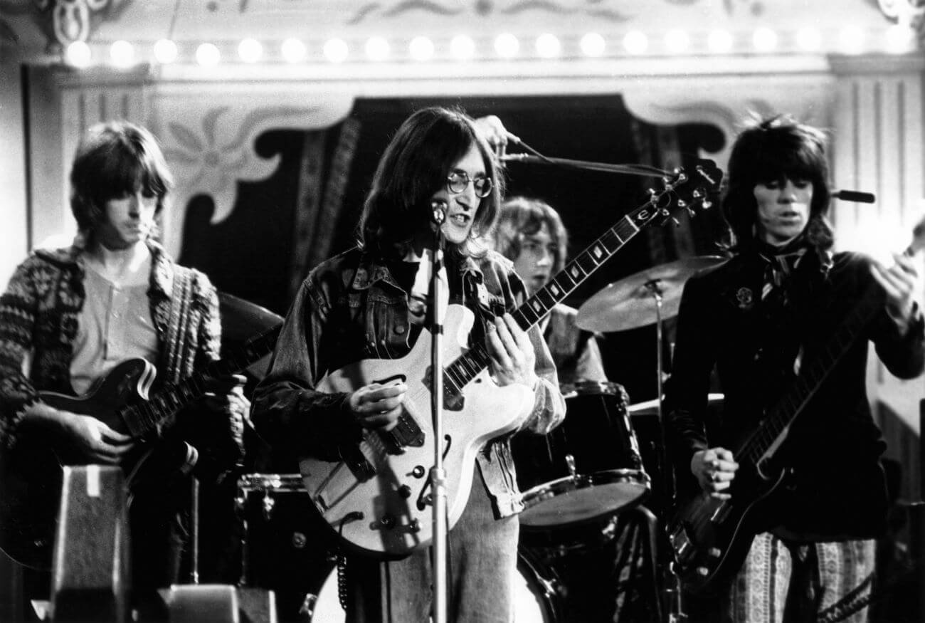A black and white picture of Eric Clapton, John Lennon, and Keith Richards playing guitars on a stage.