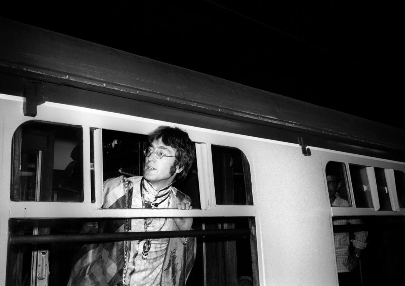 A black and white picture of John Lennon looking out the window of a train.